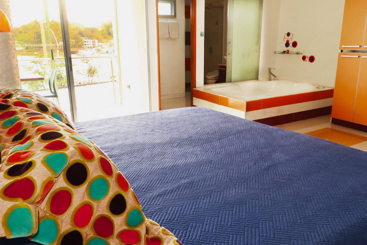 Ein Schlafzimmer mit einem großen Bett, ein Badezimmer mit einer Badewanne und Blick ins Freie.