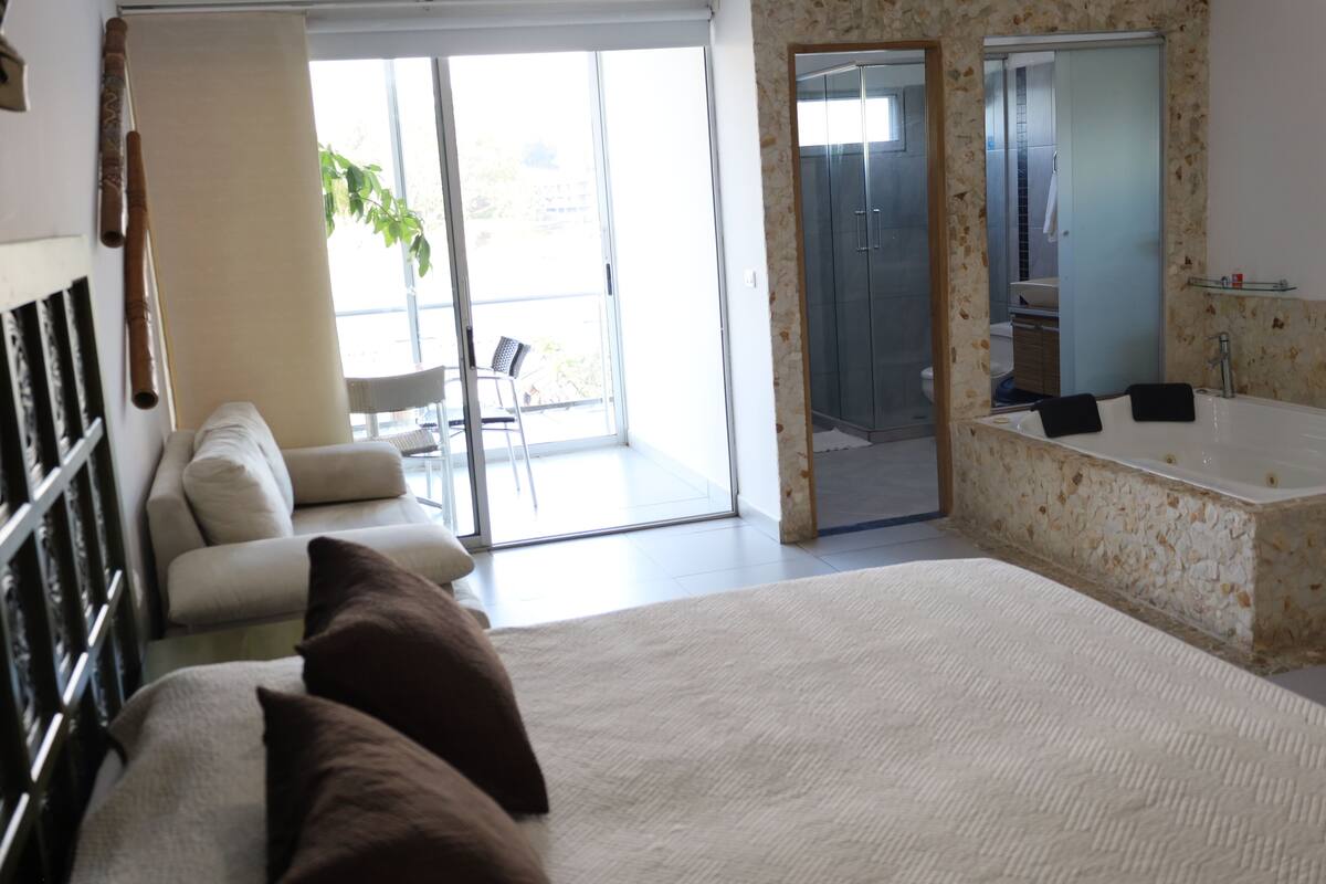 Ein Schlafzimmer mit einem großen Bett, einer Schiebetür zu einem Balkon und einem Badezimmer mit Badewanne und Dusche.