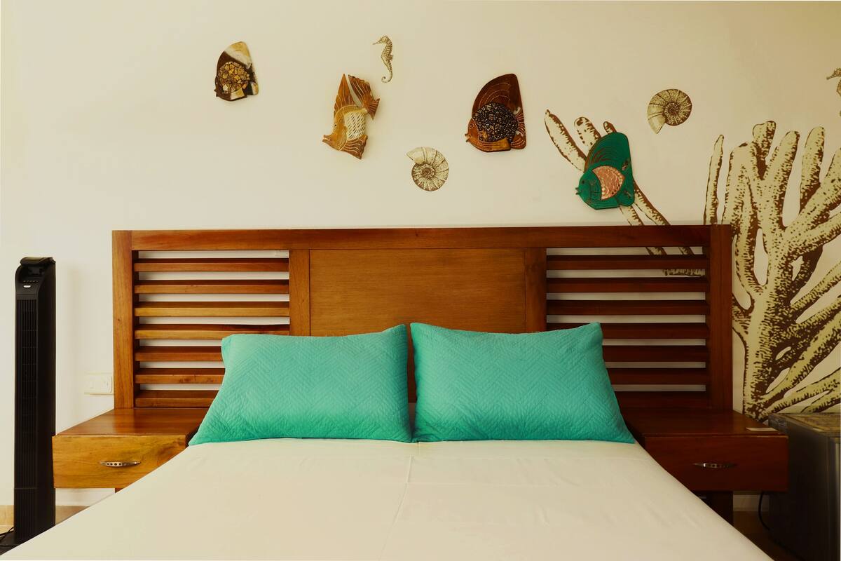 Ein Bett mit zwei türkisfarbenen Kissen, einem Holz-Kopfteil und einer Wand, die mit Muscheln und einem Seepferdchen verziert ist.