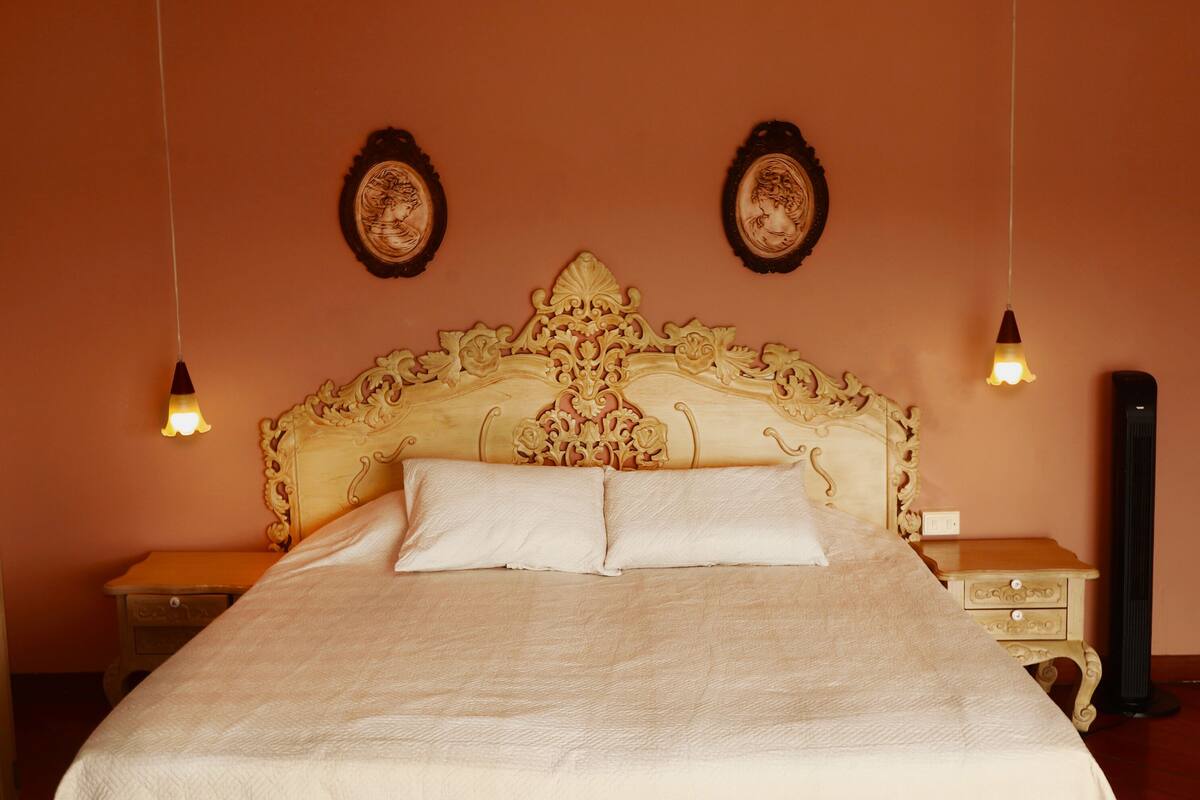 Ein Bett mit aufwendiger Kopfteile, zwei an der Wand befestigte Bilderrahmen und ein Nachttisch mit Lampe.