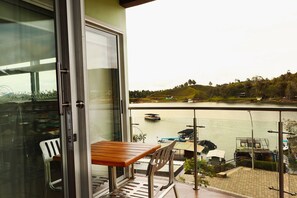 A balcony with a wooden table and chairs, overlooking a body of water with boats and a hilly landscape. - HOTEL PORTOBELO GUATAPE (Guatapé)