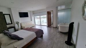 A modern bedroom with a bed, a large window, a bathroom with a bathtub, and a flat-screen TV. - HOTEL PORTOBELO GUATAPE (Guatapé)