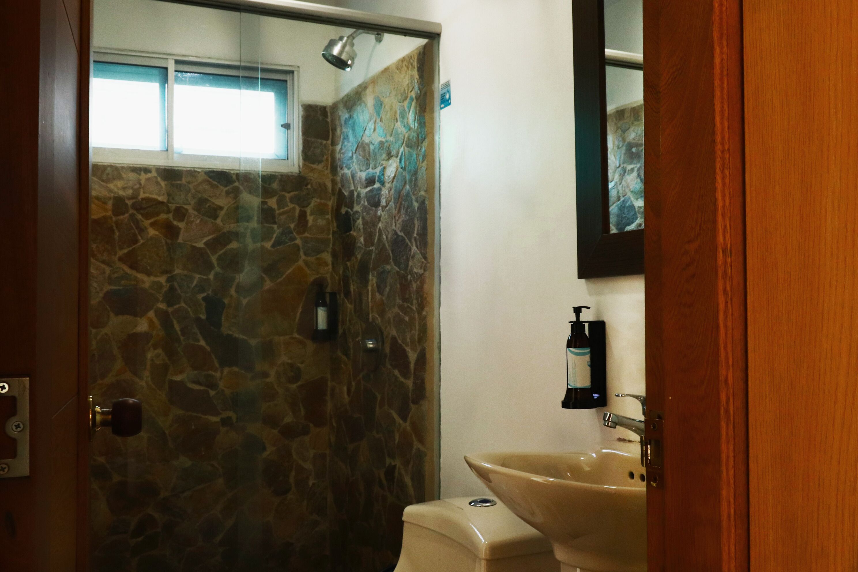 Ein Badezimmer mit einer Duschwand aus Stein, einem beigen Waschbecken und einem Spiegel darüber.