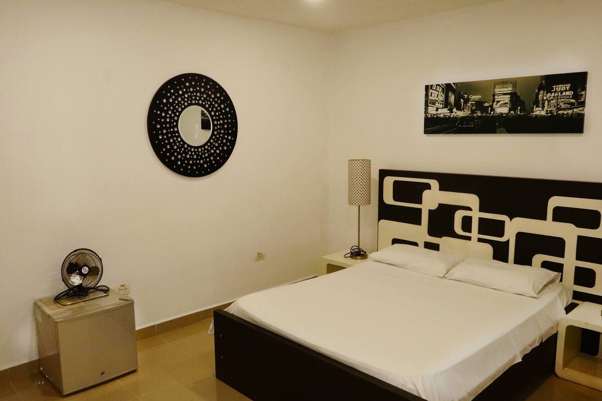Ein Schlafzimmer mit Bett, Nachttisch, Lampe, Wanduhr und Spiegel.