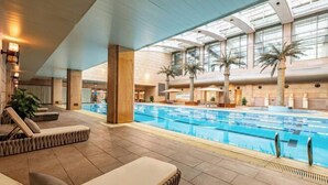 Ein Hallenbad mit Liegestühlen und Palmen.