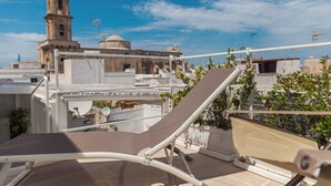 A rooftop terrace with a sun lounger, a white railing, and a view of historic buildings in the background. - Palazzo Fiscaiolo (Monopoli)