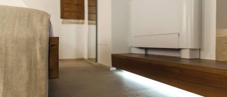 A modern hotel room with a wooden floor, a white wall, and a wooden bench.