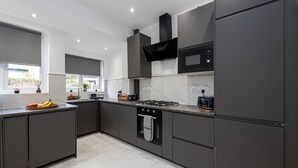 A modern kitchen with dark cabinetry, a gas stove, a microwave, and a large window. - CollegeHouse-FREEParking&HighSpeedWIFI-Modern-Cosy (Whalley Range)