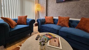 A living room with two blue sofas, brown cushions, a floor lamp, a painting, and a magazine on a coffee table. - CollegeHouse-FREEParking&HighSpeedWIFI-Modern-Cosy (Whalley Range)