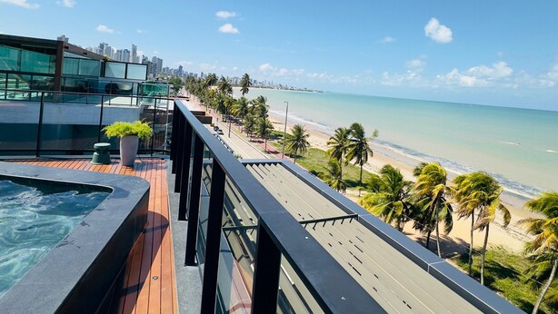 Une terrasse sur le toit avec une piscine, des palmiers et une vue sur la plage et l’océan.
