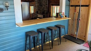 A bar area with a stone wall, wooden counter, and three stools. - Adorable Lakefront Cabin with HOT TUB! (Gresham)