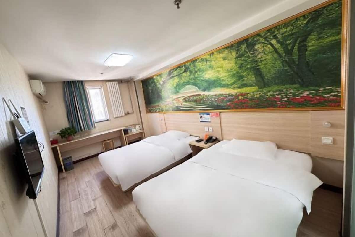 Habitación de hotel con dos camas, un escritorio, un televisor y un gran mural de un bosque en la pared.