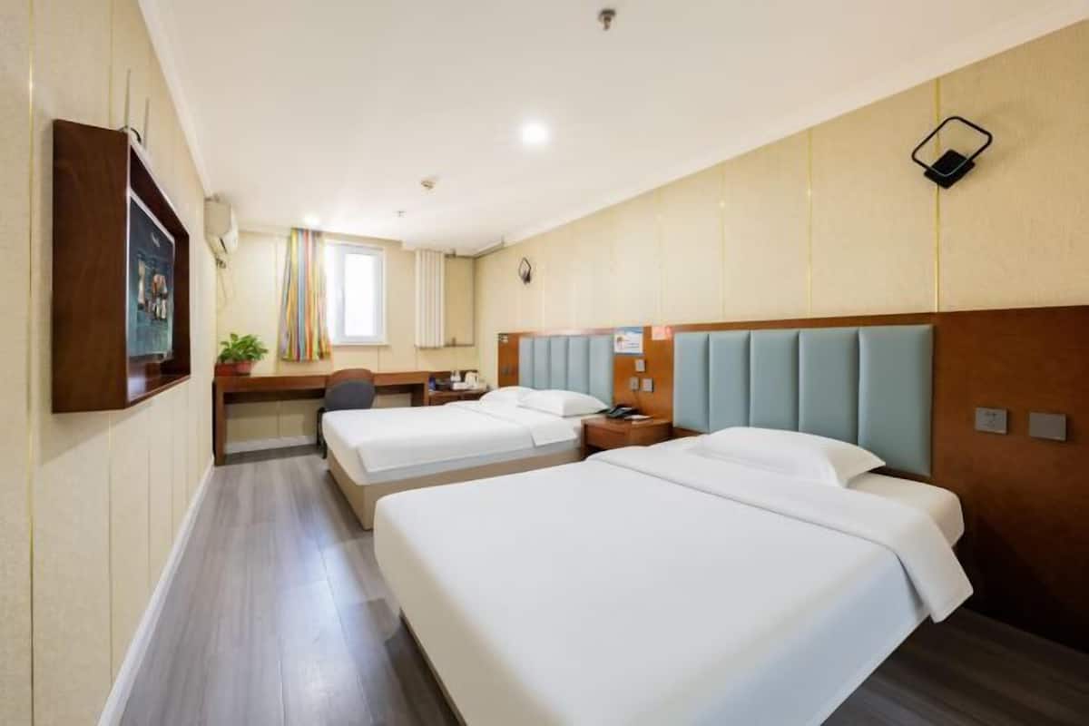 Habitación de hotel con dos camas, un escritorio, una silla, una mesita y una ventana con cortinas.