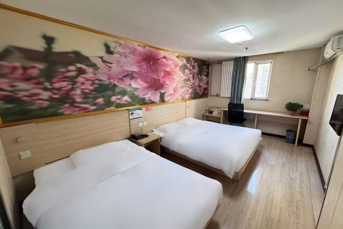 Habitación de hotel con dos camas, un escritorio, una silla, un televisor y un mural floral grande.