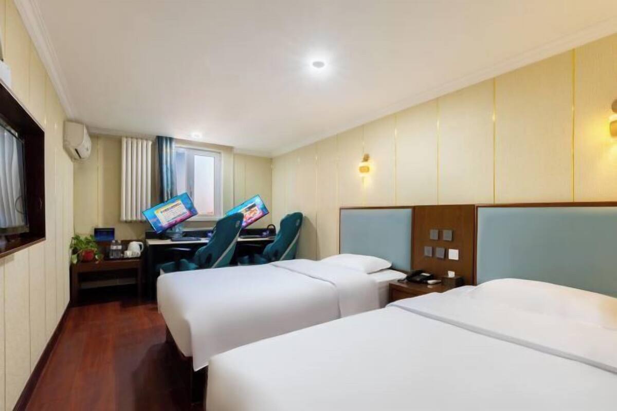 Una habitación de hotel con dos camas, un escritorio con computadora, una silla y un ventanal con cortinas.