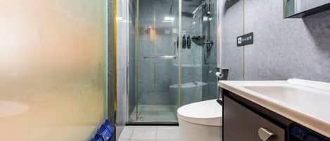 Un baño con cabina de ducha de vidrio, inodoro y lavamanos con armario.