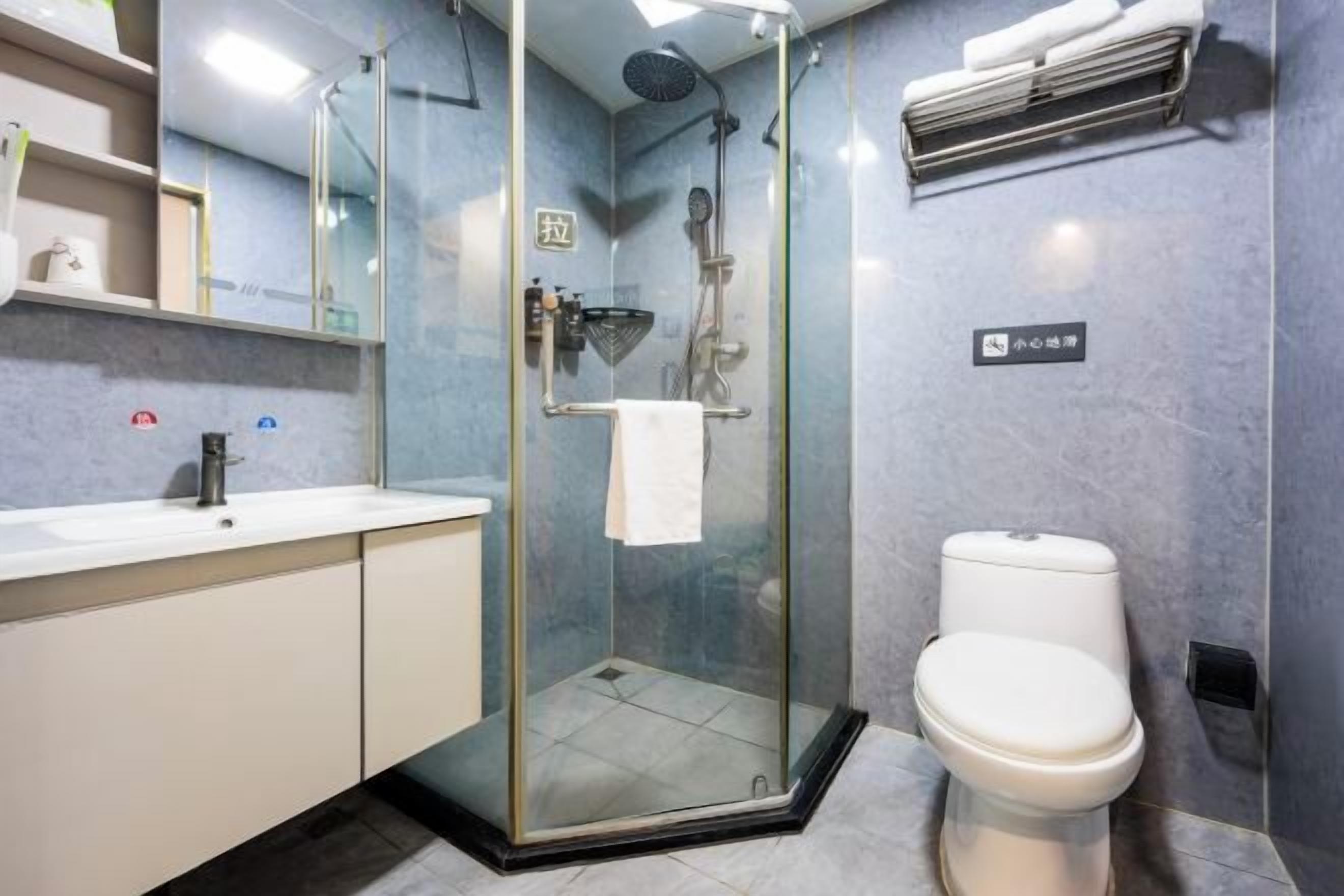 Un baño moderno con ducha envuelta en vidrio, inodoro blanco y lavamanos con espejo arriba.