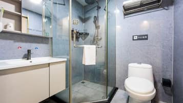 Un baño moderno con ducha envuelta en vidrio, inodoro blanco y lavamanos con espejo arriba.
