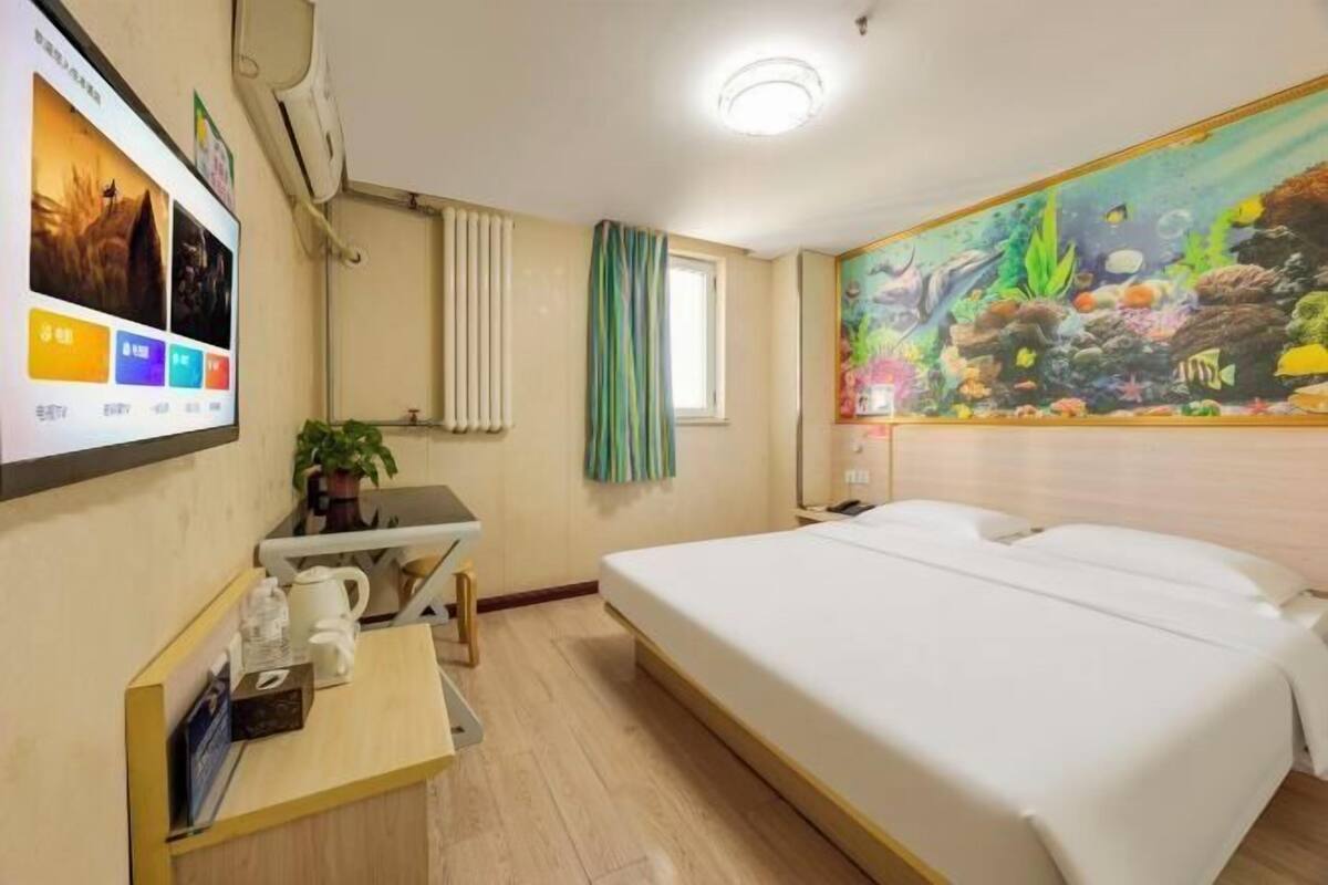 Habitación de hotel con una cama, un escritorio con computadora, un televisor montado en la pared y un cuadro grande de una escena submarina.