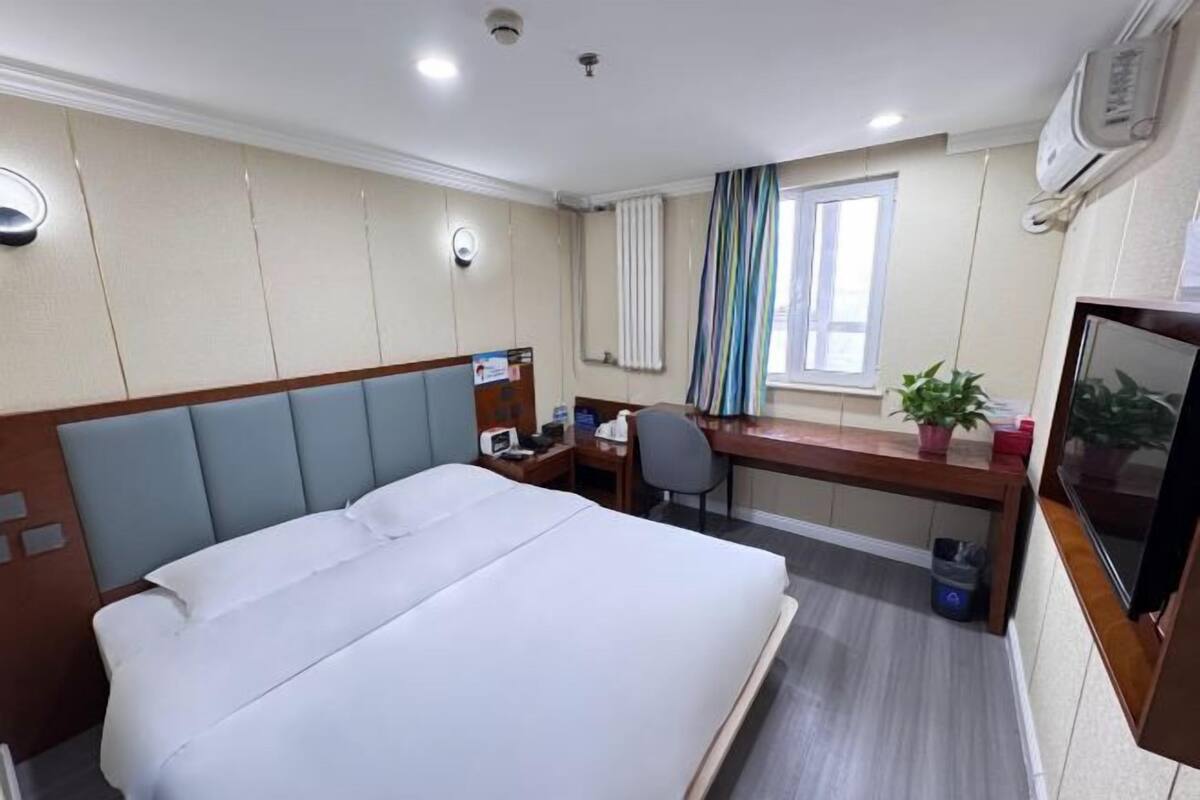 Habitación de hotel con cama, escritorio, silla, televisión y ventana con cortinas.