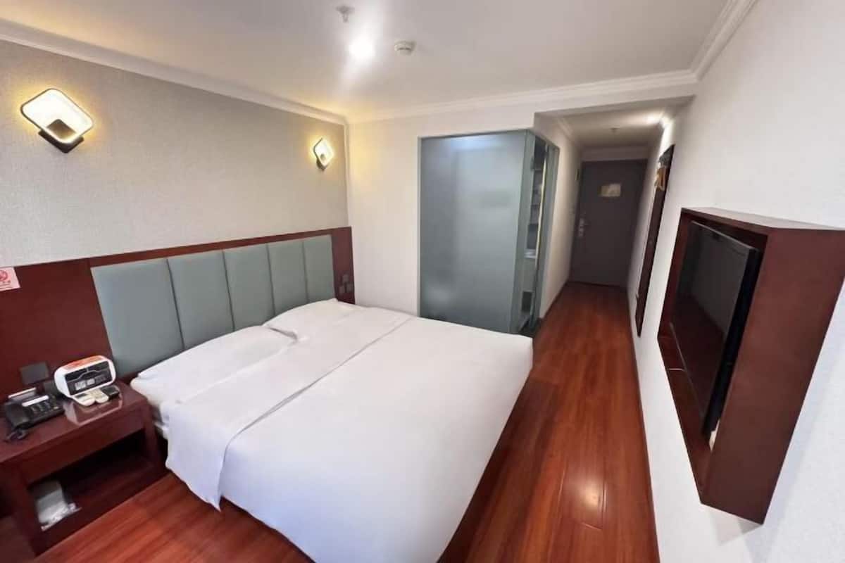 Habitación de hotel con cama, mesita de noche, lámpara y televisor montado en la pared.