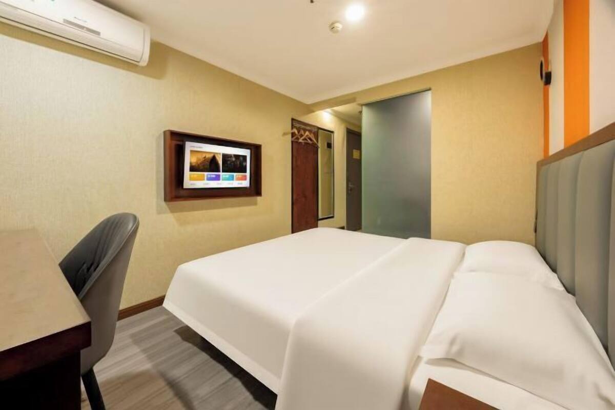 Una habitación de hotel con cama, escritorio y silla. Hay un televisor montado en la pared y una puerta que da a otra habitación.