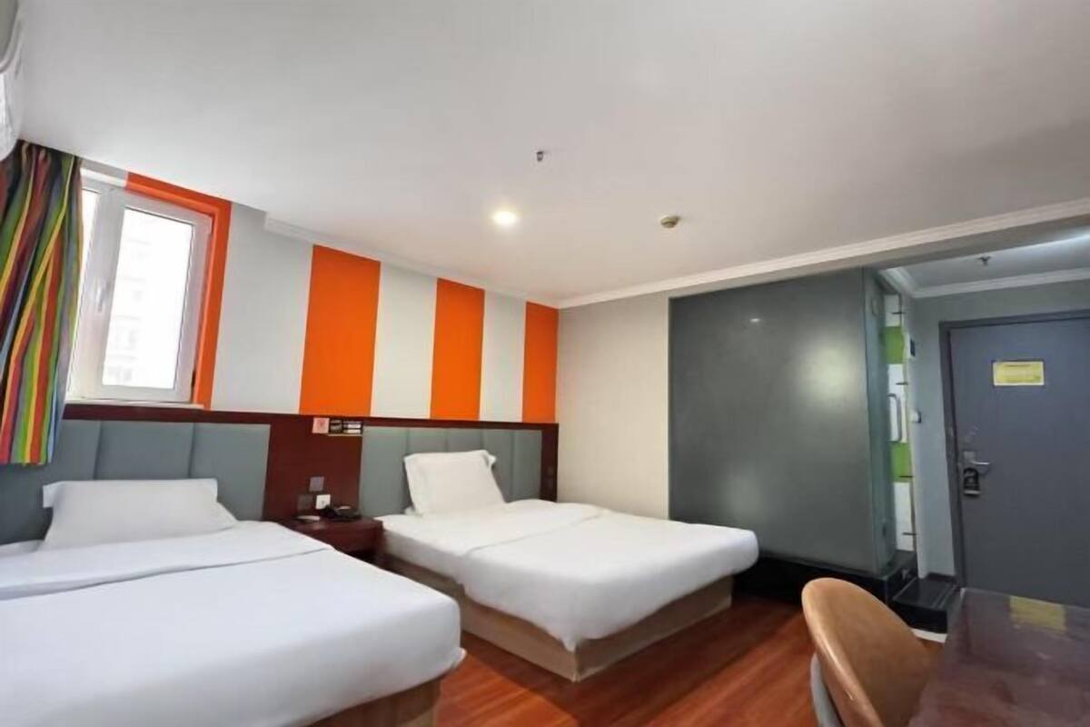 Habitación de hotel con dos camas, una ventana con cortinas y una puerta.