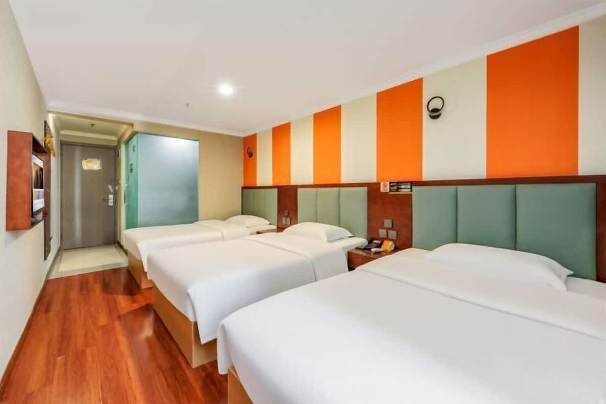 Habitación de hotel con tres camas individuales, suelo de madera y diseño de pared a rayas.