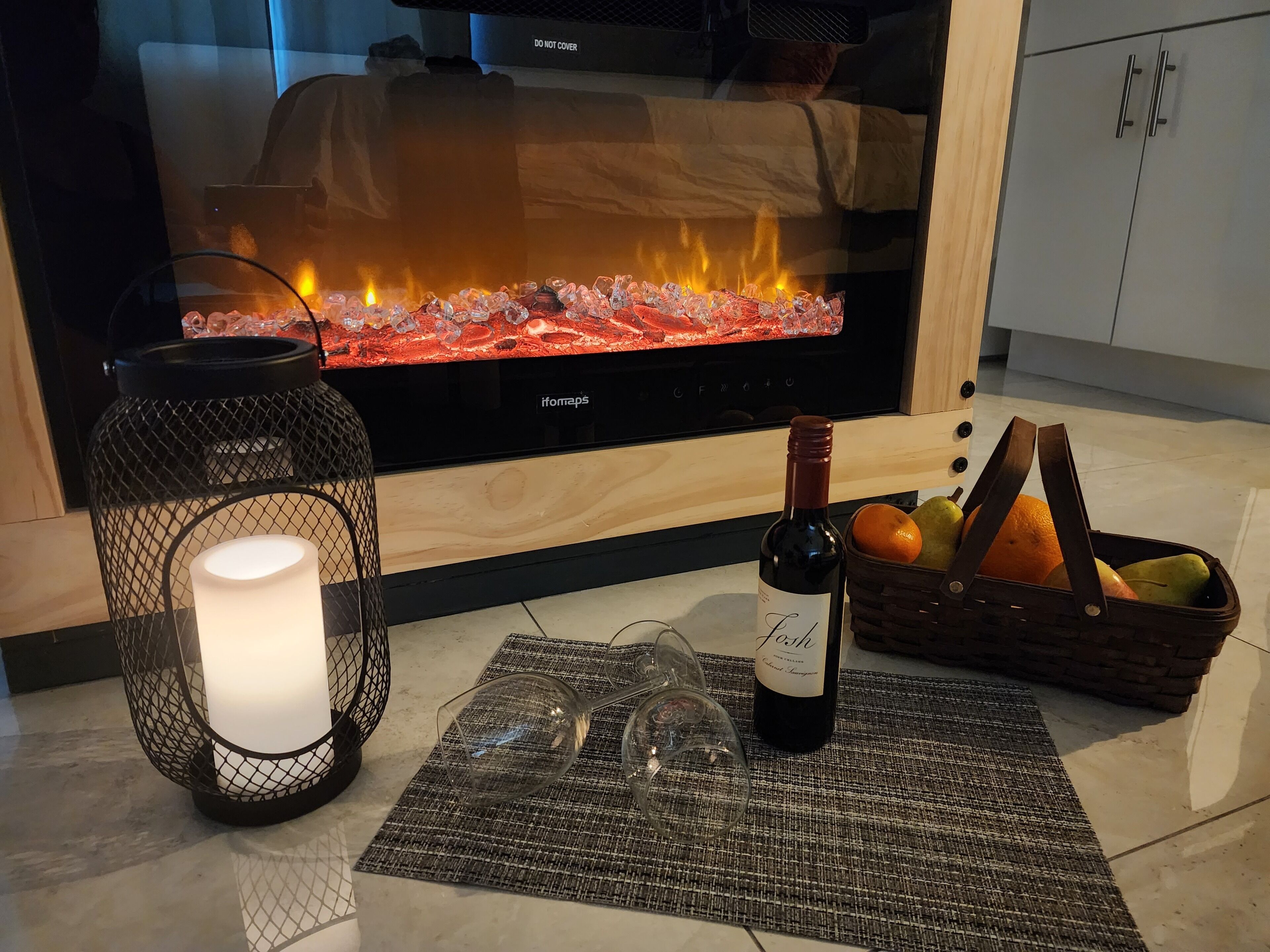 Ein gemütliches Wohnzimmer mit Kamin, brennender Kerze, Weinflasche und Obstkorb.