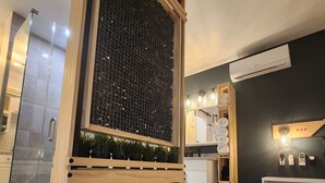 A modern bathroom with a glass shower enclosure, a wooden vanity with a built-in sink, and a wall-mounted air conditioning unit. - Cozy Apartment at Citrus Park (Tampa)