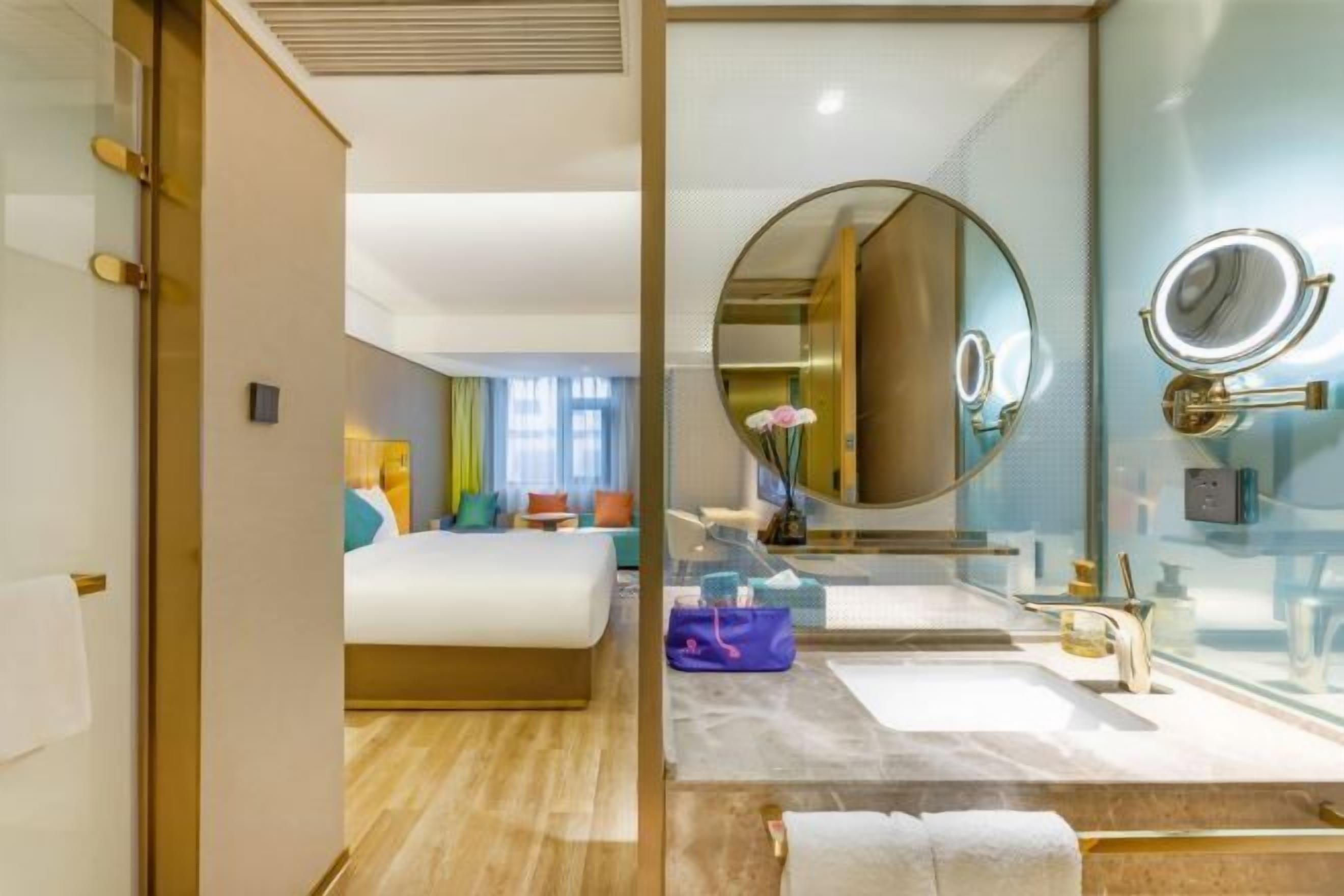 Ein modernes Hotelzimmer mit einem großen Bett, einem Badezimmer mit rundem Spiegel und Blick auf die Stadt.