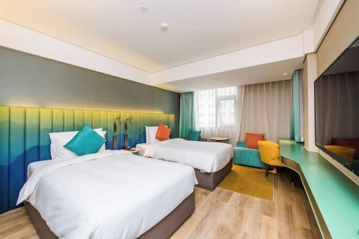 A hotel room with two beds, a sofa, a small table, and a mirror.