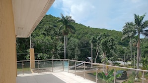 A balcony with a tiled floor, metal railing, and a view of a lush green hillside with palm trees. - Blue Seas Two Unity Hall (Montego Bay)