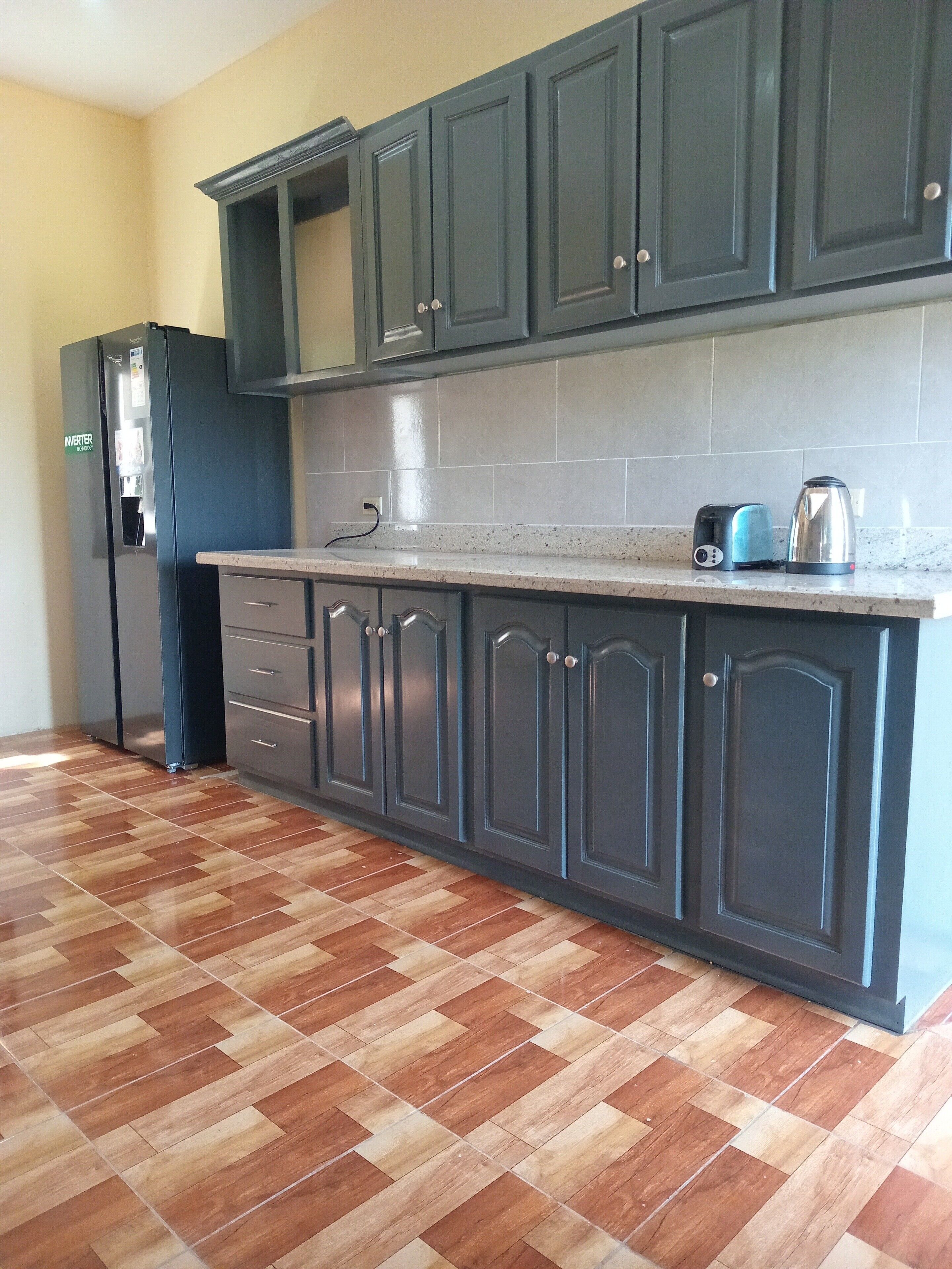 A kitchen with dark cabinets, a refrigerator, a toaster, and a kettle on the countertop.
