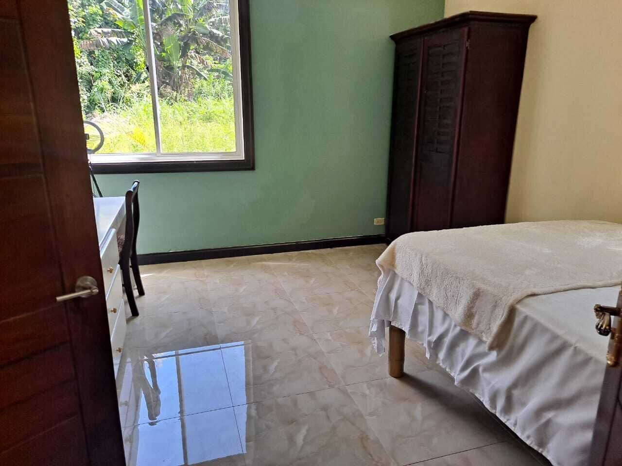 A bedroom with a bed, a wardrobe, a desk, and a window with a view of greenery.