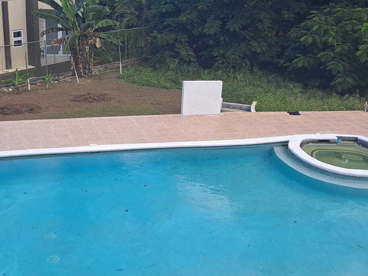 Una piscina con solárium de baldosas, un hidromasaje pequeño y circular, y una silla blanca.