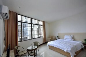 A hotel room with a bed, a chair, a small table, and a window with curtains. - Huangyao Xinyi Inn (Zhaoping)