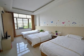 Quarto de hotel com três camas, uma escrivaninha, uma cadeira, um guarda-roupa e uma janela com cortinas.