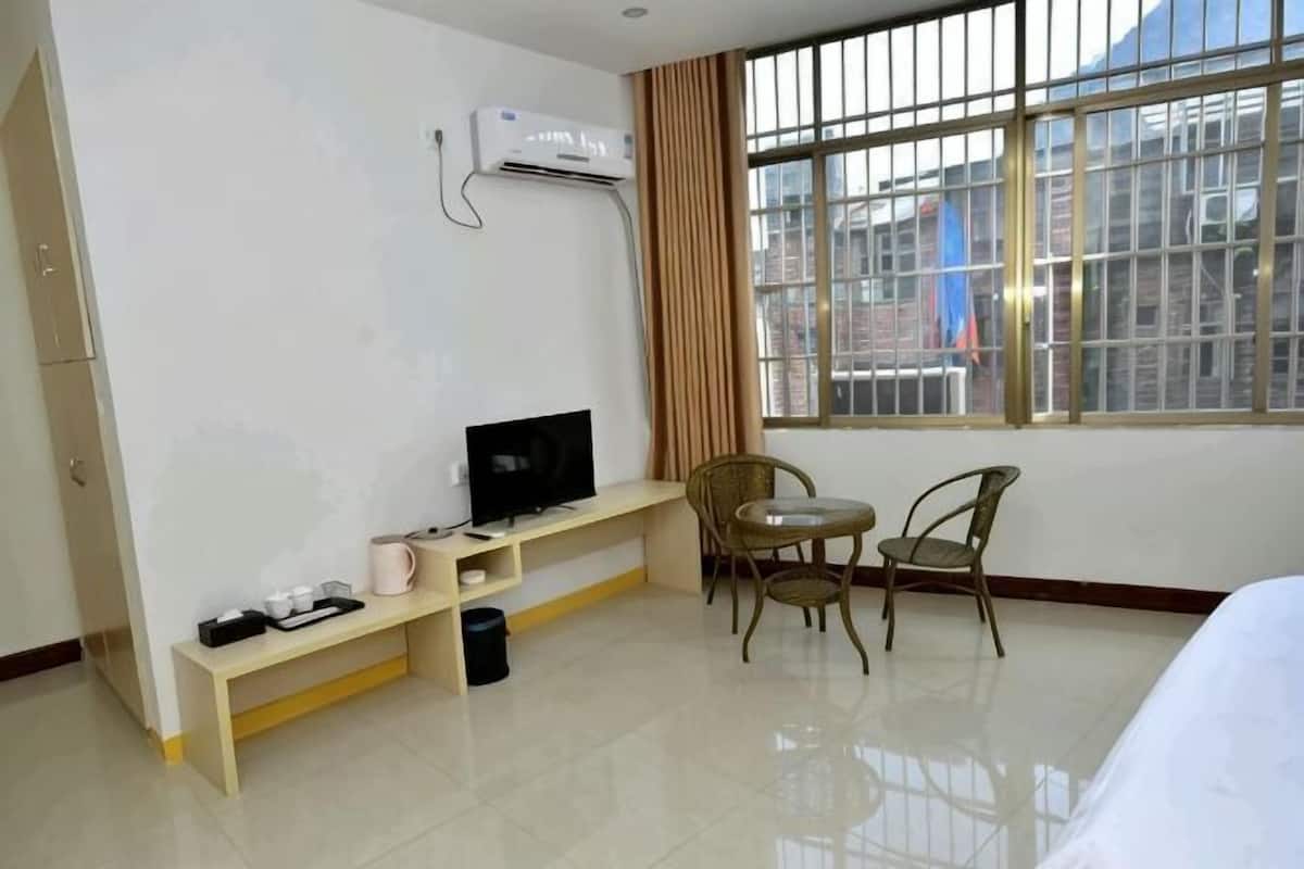 A hotel room with a bed, a TV on a stand, a window with curtains, and a chair.