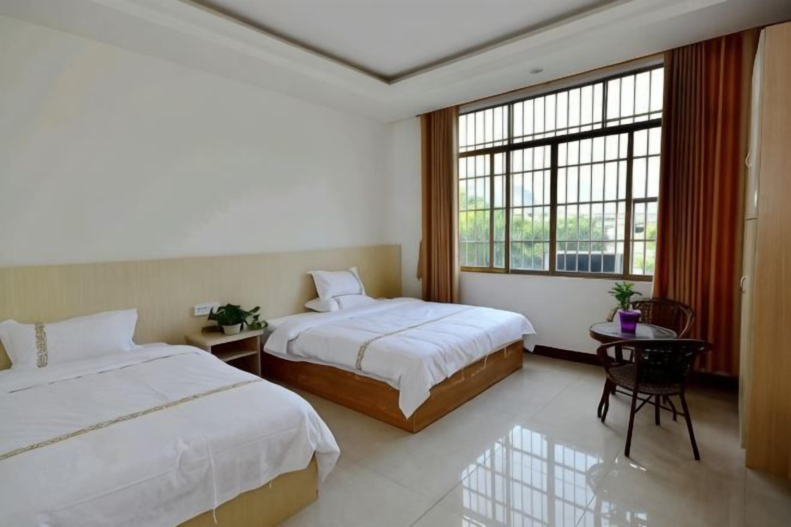 A hotel room with two beds, a small table, and a window with curtains.