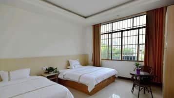 A hotel room with two beds, a small table, and a window with curtains.