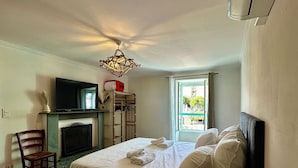 A bedroom with a bed, a TV, a fireplace, a chair, and a window with a view. - Casa Marelina - Fisherman's house in Centuri harbour (Centuri)