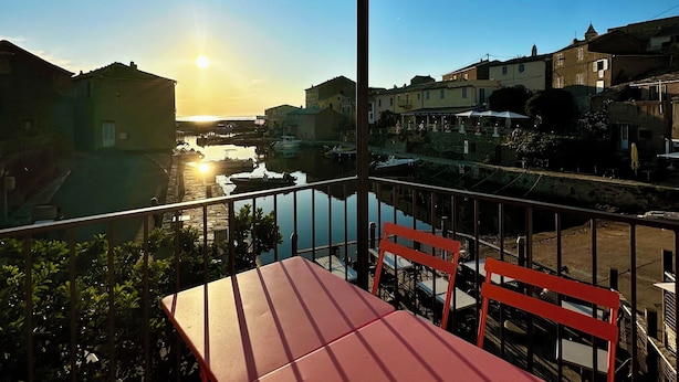A balcony with a table and chairs, overlooking a canal with buildings and boats. - Casa Marelina - Fisherman's house in Centuri harbour (Centuri)