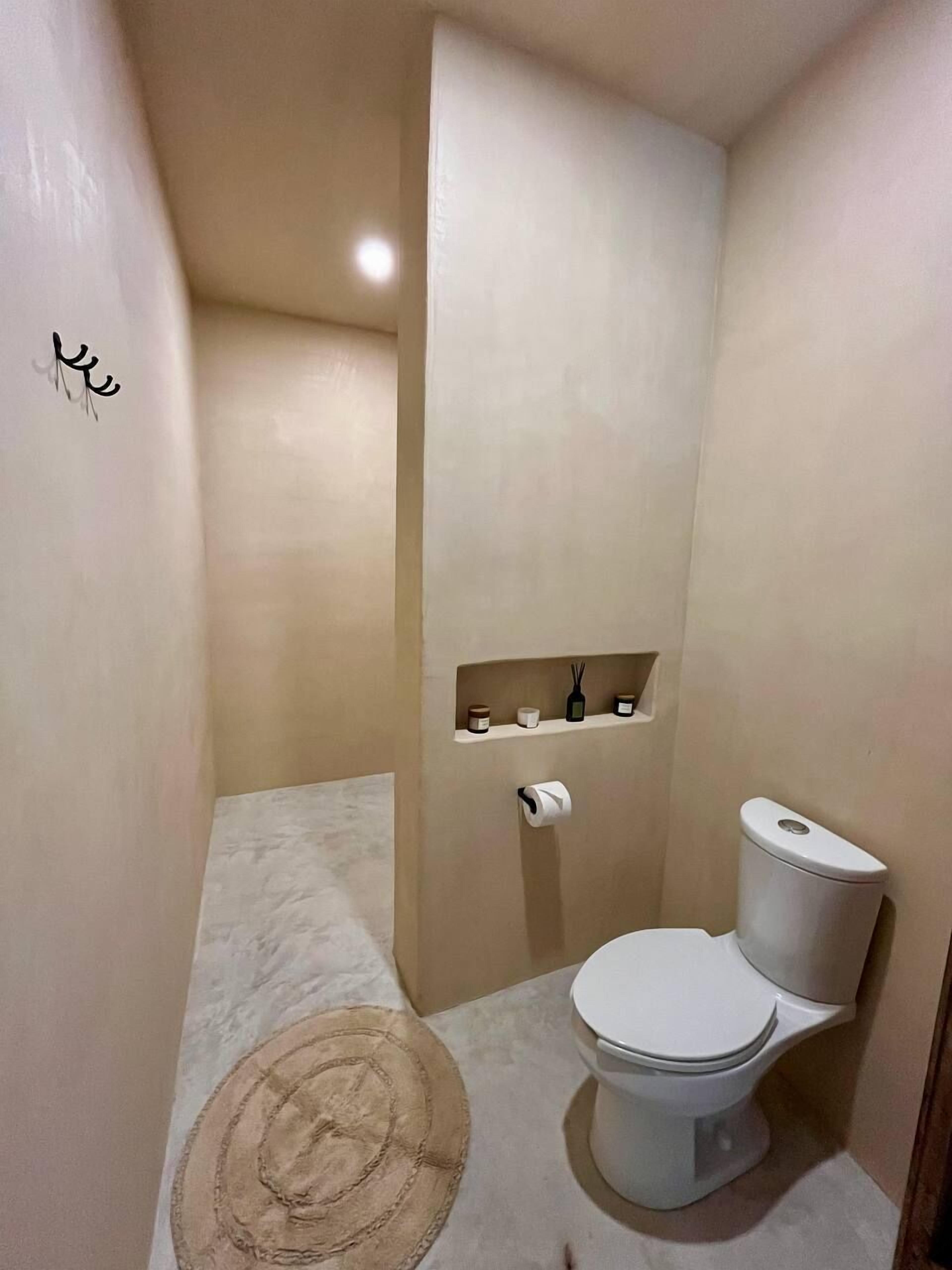 Ένα μικρό, μοντέρνο μπάνιο με τουαλέτα, μια κρεμάστρα για πετσέτες και ένα ράφι με είδη προσωπικής υγιεινής.
