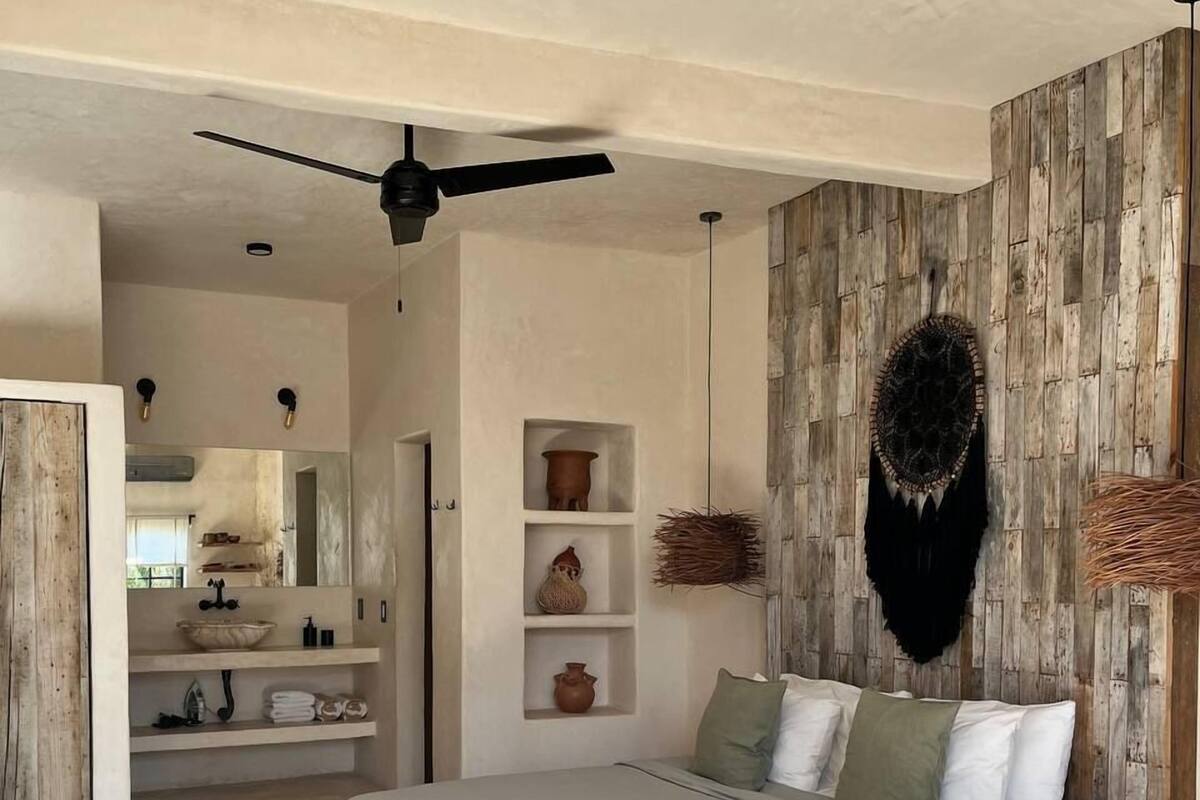 A bedroom with a bed, a ceiling fan, shelves with decorative items, and a wooden accent wall.