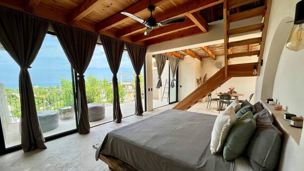 Ein Schlafzimmer mit einem großen Bett, Blick ins Freie und einer Holztreppe.