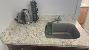 Een keuken met een granieten aanrecht, een koffiezetapparaat, een glazen vaas en een groene gootsteen.