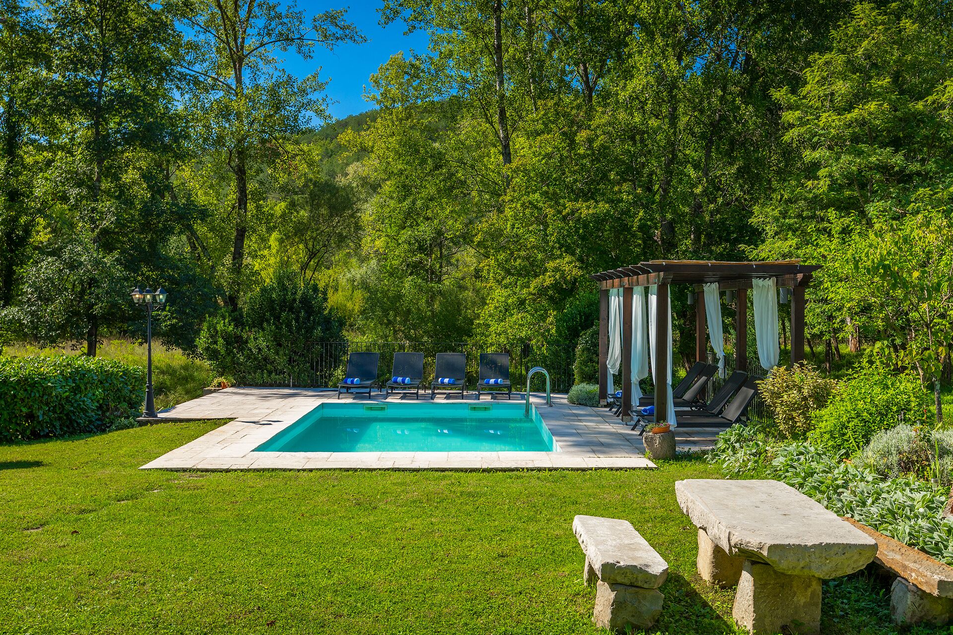 A rectangular swimming pool with a pergola and lounge chairs in a lush garden setting.