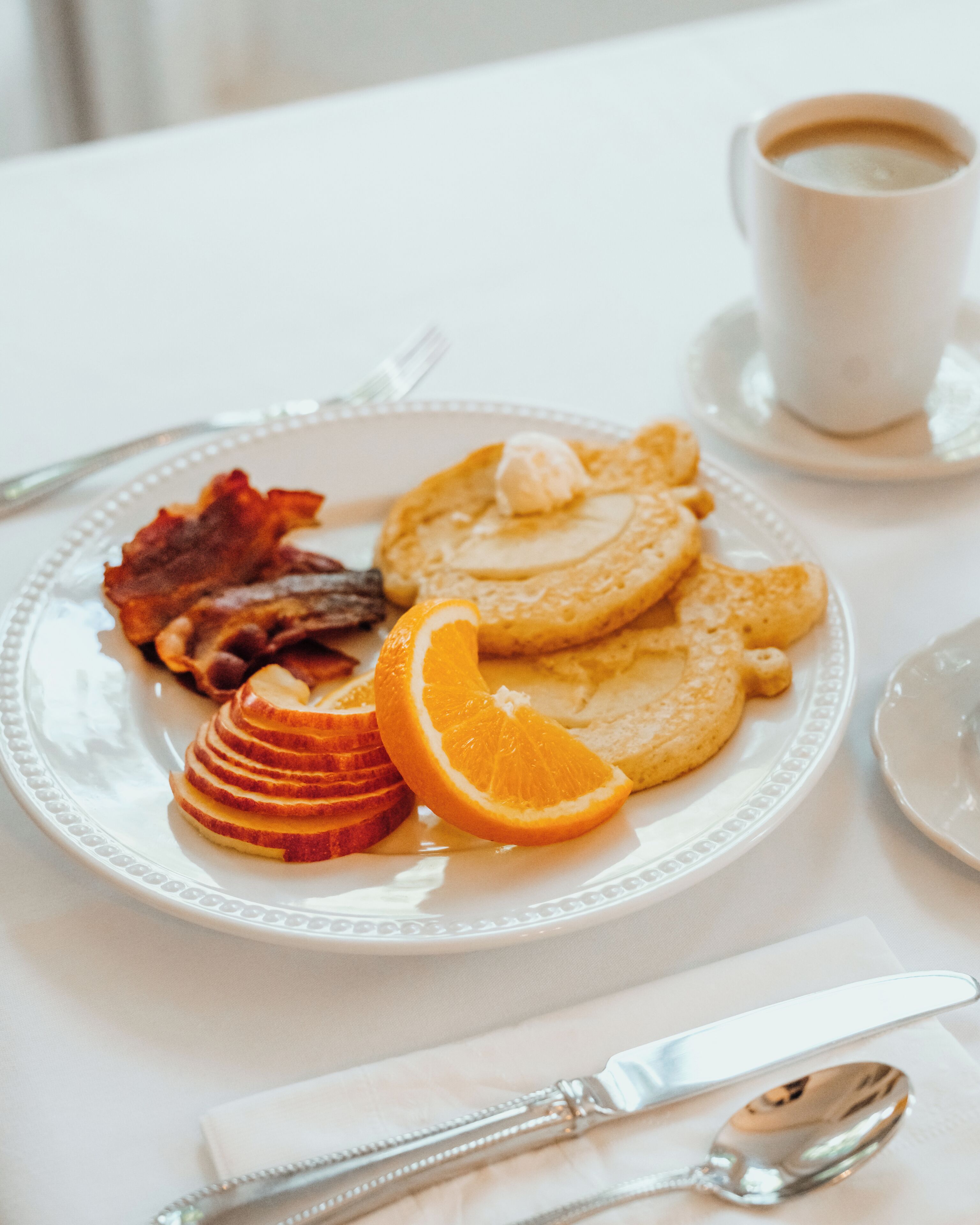 A breakfast plate with pancakes, bacon, orange slices, and a cup of coffee.
