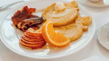 A breakfast plate with pancakes, bacon, orange slices, and a cup of coffee.